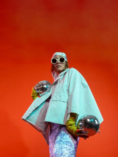 femme-debout-tient-boules-disco-lunettes-soleil-fonds-rouge